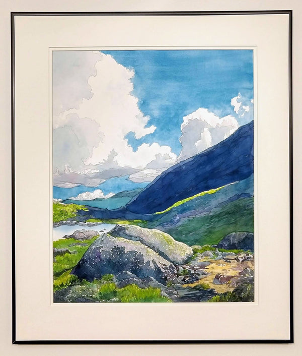 "Alpine Light" is a 16 by 20 inch watercolor and ink painting on paper by Rebecca M. Fullerton, depicting Star Lake, the slopes of Mount Adams, and glimpses of the Presidential Range in the White Mountain National Forest of New Hampshire. Huge white clouds move over blue mountains, green alpine plants and craggy granite boulders on the edge of a mountain pond. This view shows the painting in its frame.