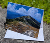 Greeting card with a mountain landscape and blue sky on a stone surface.