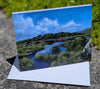 Greeting card with a scenic landscape of a lake and mountains on a stone surface.
