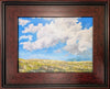 Framed painting of clouds drifting over an alpine mountain slope with blue skies beyond.
