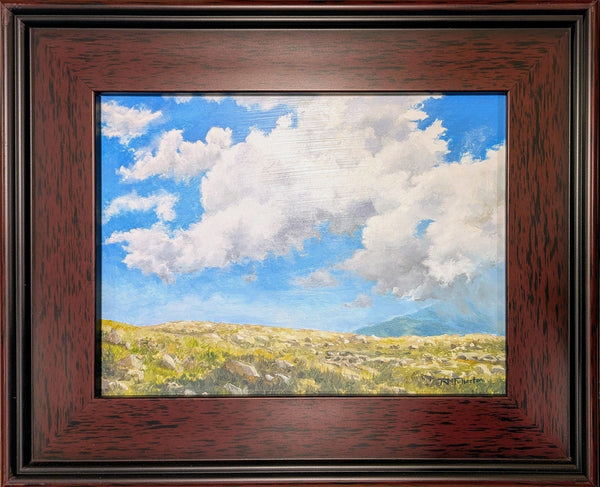 Framed painting of clouds drifting over an alpine mountain slope with blue skies beyond.
