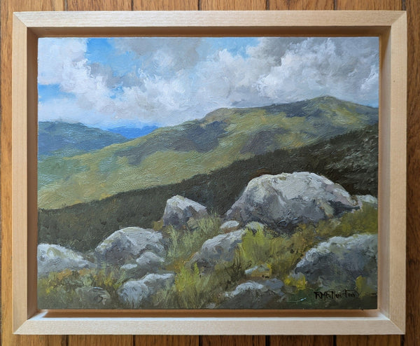 Painting of a mountain landscape with rocks and clouds in a wooden frame.