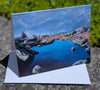 Scenic greeting card with a lake and rocky landscape on a stone surface.