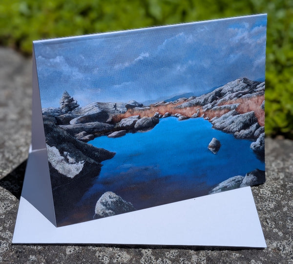 Scenic greeting card with a lake and rocky landscape on a stone surface.