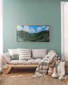"Mount Willard, Summer" is a 20 by 40 inch framed oil on canvas painting by Rebecca M. Fullerton depicting the view over Crawford Notch from Mount Willard in the heart of New Hampshire's White Mountains. This artwork depicts mountains, valleys, forests, cliffs, trees, roads, railroad tracks, clouds, blue sky and summertime. This is the painting hung in a cozy living room.