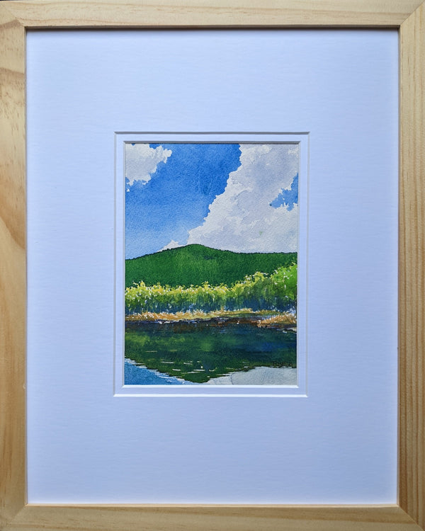 "Summer Idyll" is a 5 by 7 inch watercolor and ink painting by White Mountains artist Rebecca M. Fullerton, depicting a hill and puffy clouds reflected in a mountain pond.